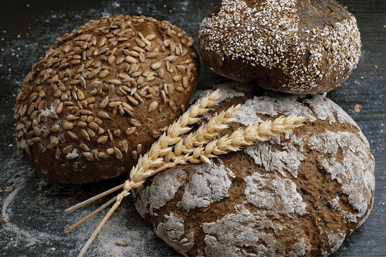 Three pieces of wheat laying against three round loaves of artisanal bread.