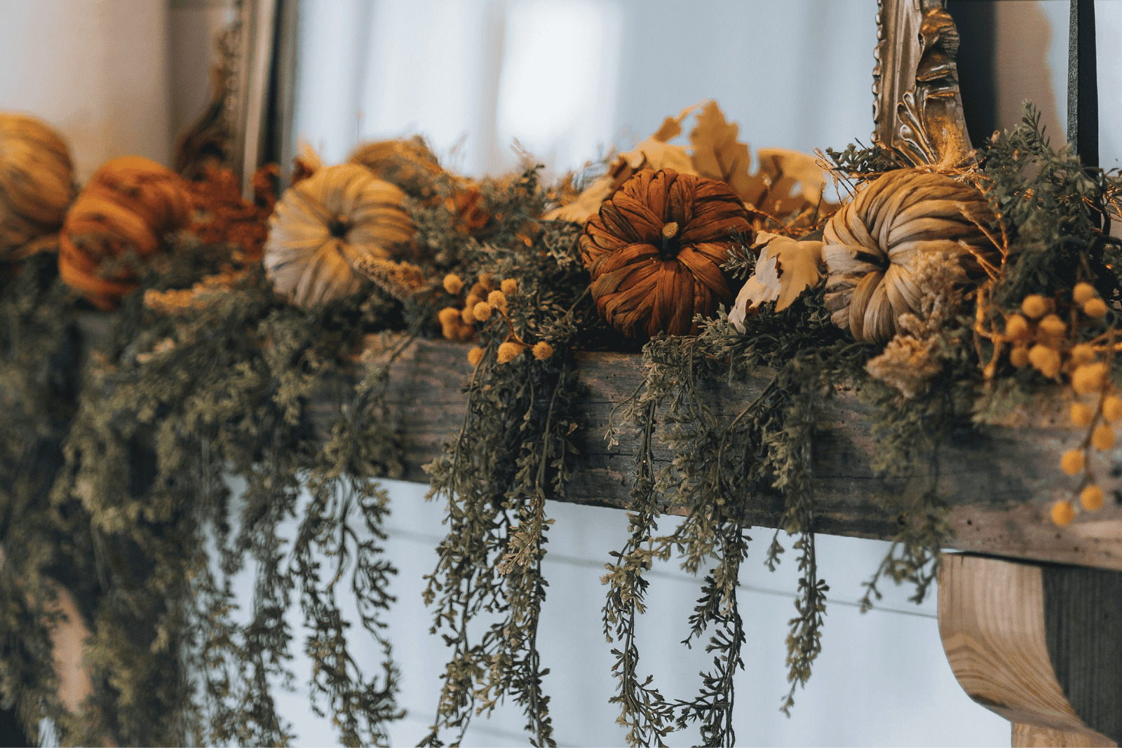 A wooden mantle decorated with evergreen boughs, mini pumpkins, and dried berries.