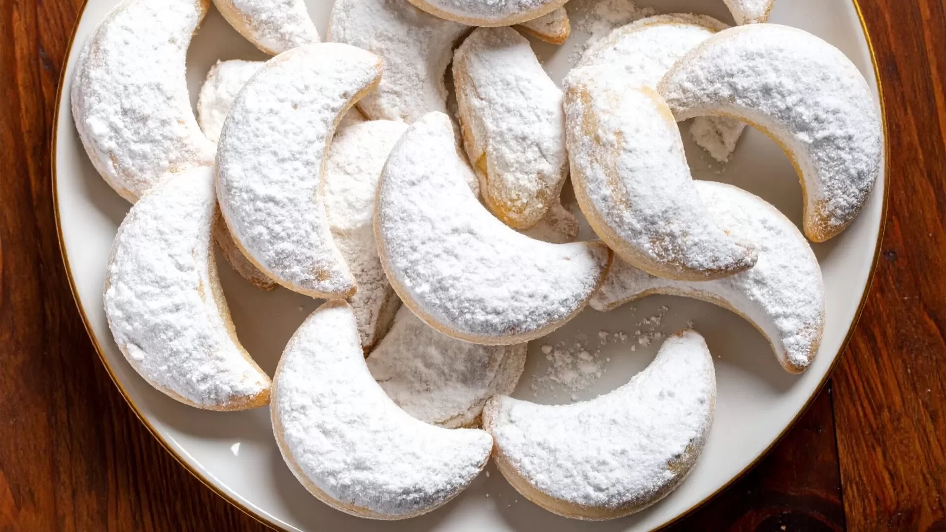 A plate of crescent-shaped Kourabiedes, Greek butter cookies, on a wooden background